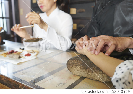 Chinese medicine practitioner taking pulse of customer Chinese medicine practitioner taking pulse of customer 58910509
