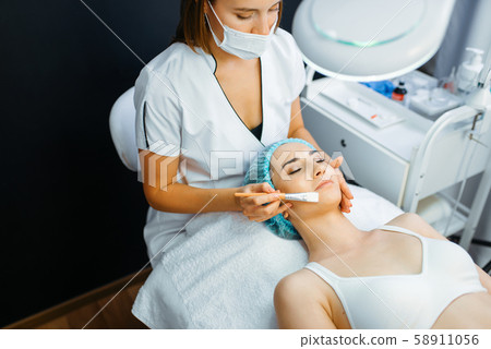 Cosmetician with brush cleans facial skin Cosmetician with brush cleans facial skin 58911056
