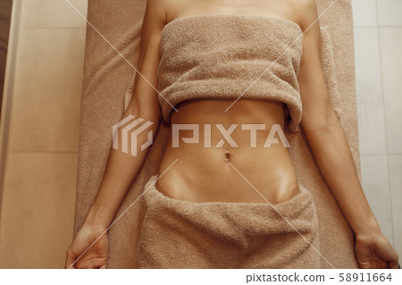 Slim woman in towel lying on massage table Slim woman in towel lying on massage table 58911664