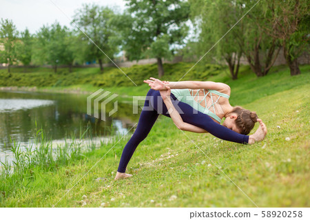 A young sports girl practices yoga on a green lawn A young sports girl practices yoga on a green lawn 58920258