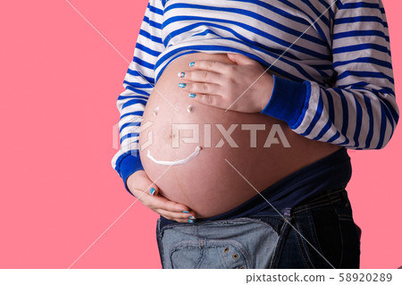 Pregnant woman writing 'smiley' word on her belly. Trendy Pink background. Pregnant woman writing 'smiley' word on her belly. Trendy Pink background. 58920289