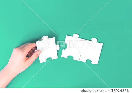 Hand holding a jigsaw puzzle piece on green 58929888