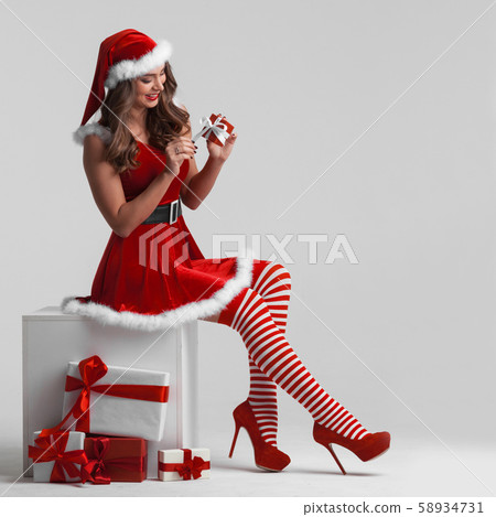 Girl in santa dress unwrapping gift 58934731