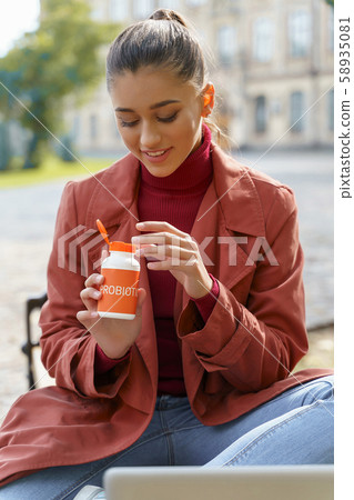 Cheerful woman taking probiotics sitting in the park 58935081