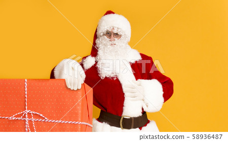Santa Claus standing with big gift box over orange Santa Claus standing with big gift box over orange 58936487