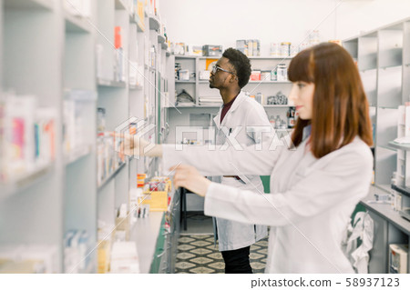 Portrait of a young Caucasian female pharmacist, male African colleague working with drugs in the Portrait of a young Caucasian female pharmacist, male African colleague working with drugs in the 58937123