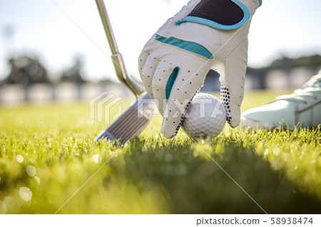 Hand in glove placing golf ball on tee Hand in glove placing golf ball on tee 58938474