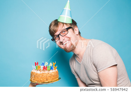 Funny crazy young student in a greeting hat rejoices next to the cake with the inscription happy Funny crazy young student in a greeting hat rejoices next to the cake with the inscription happy 58947942