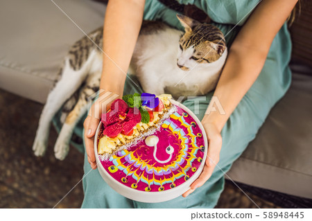 Young woman having a mediterranean breakfast seated at her sofa and with her cat and eats Healthy 58948445