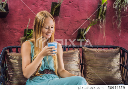 Young woman having a mediterranean breakfast seated at sofa and drinks Trendy drink: Blue latte. Hot 58954859