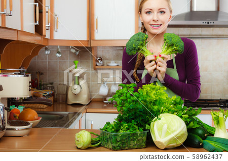 Woman in kitchen with green vegetables broccoli in 58962437