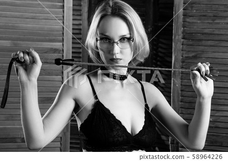 Sexy blond dominant woman holds whip over wooden folding panel 58964226
