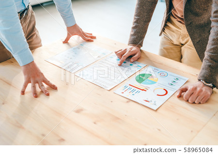 Two young economists in formalwear bending over financial papers on wooden table 58965084