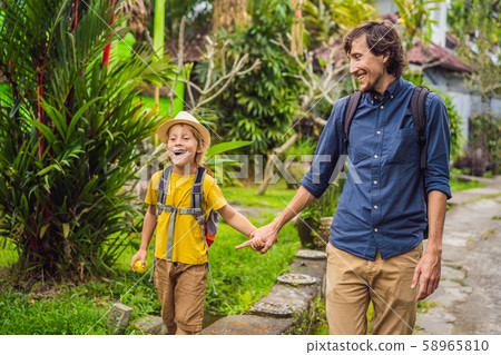 Father and son tourists in Bali walks along the narrow cozy streets of Ubud. Bali is a popular Father and son tourists in Bali walks along the narrow cozy streets of Ubud. Bali is a popular 58965810