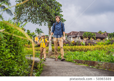 Father and son tourists in Bali walks along the narrow cozy streets of Ubud. Bali is a popular Father and son tourists in Bali walks along the narrow cozy streets of Ubud. Bali is a popular 58965889