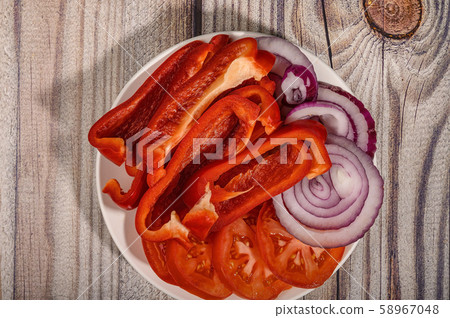 Sliced tomatoes, sweet peppers and onions in a plate on a wooden table. 58967048