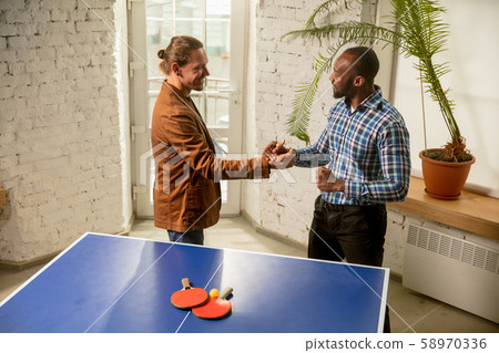 Young men playing table tennis in workplace, having fun Young men playing table tennis in workplace, having fun 58970336