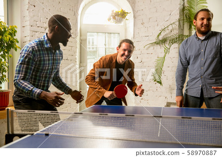 Young people playing table tennis in workplace, having fun Young people playing table tennis in workplace, having fun 58970887
