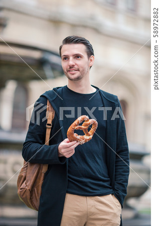 Beautiful young man holding pretzel and relaxing in park Beautiful young man holding pretzel and relaxing in park 58972882