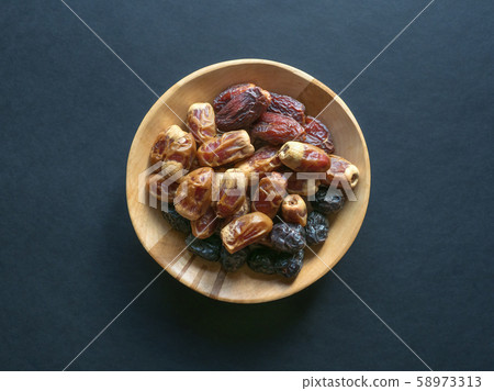 Dates in a wooden bowl on a black background. Dates in a wooden bowl on a black background. 58973313