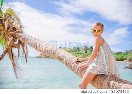 Adorable little girl sitting on palm tree during summer vacation on white beach 58973433