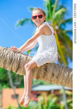 Adorable little girl sitting on palm tree during summer vacation on white beach 58973988