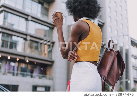 Back view of a slim lady with bag and coffee posing in urban setting Back view of a slim lady with bag and coffee posing in urban setting 58974476