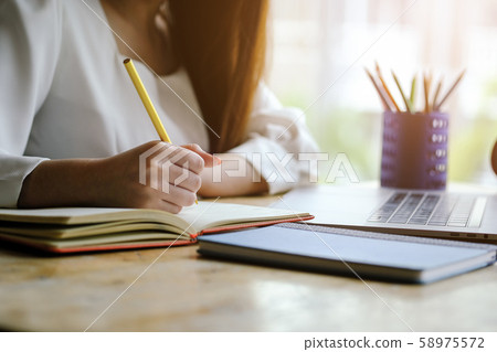 Woman hand with pencil writing on notebook. making notes in notebook with pencil. People writing on notebook and work on wooden table 58975572