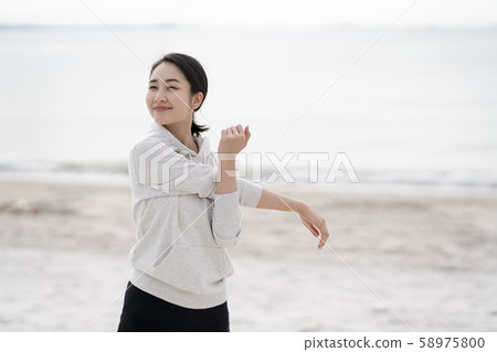 Smiling woman doing flexible exercises on sandy beach Smiling woman doing flexible exercises on sandy beach 58975800
