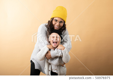 A young and energetic mother hugs and kisses her son on an orange background 58976975