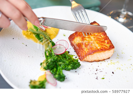 Lunch in a restaurant, a woman cuts the Salmon steak fillet and garnished with young broccoli 58977927