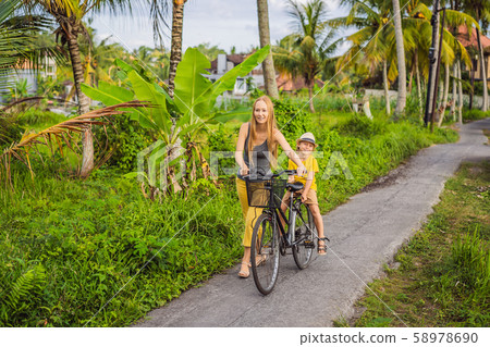 Mother and son ride a bicycle on a rice field in Ubud, Bali. Travel to Bali with kids concept Mother and son ride a bicycle on a rice field in Ubud, Bali. Travel to Bali with kids concept 58978690