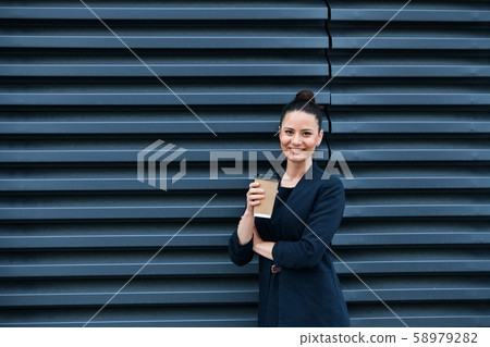 A businesswoman with coffee standing on a terrace, looking at camera. 58979282