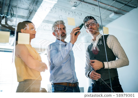 A group of business people standing in an office, brainstorming. 58979301