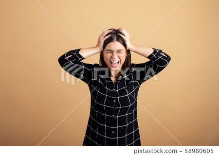 A young woman in a plaid dress stands on an orange background and shows different emotions 58980605