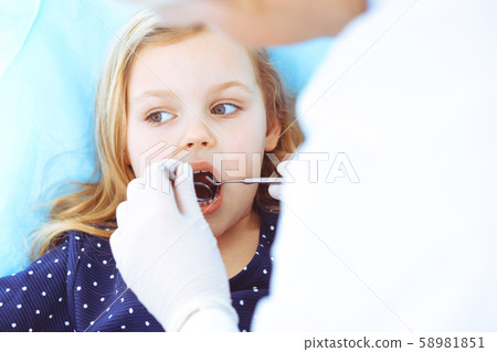 Little baby girl sitting at dental chair with open mouth during oral check up while doctor. Visiting Little baby girl sitting at dental chair with open mouth during oral check up while doctor. Visiting 58981851