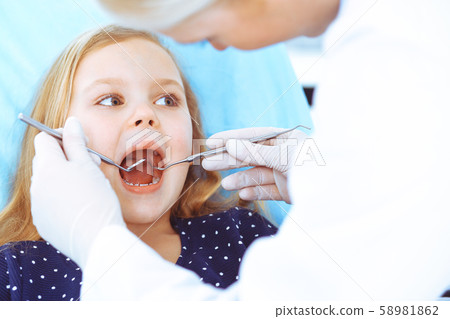 Little baby girl sitting at dental chair with open mouth during oral check up while doctor. Visiting Little baby girl sitting at dental chair with open mouth during oral check up while doctor. Visiting 58981862