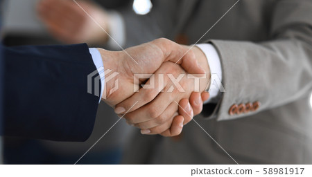 Business people shaking hands while standing with colleagues after meeting or negotiation, close-up 58981917