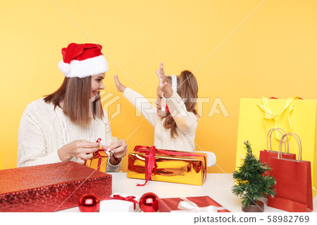 Girl with mother sitting together at the desk with presernts isolated over the yellow background. Girl with mother sitting together at the desk with presernts isolated over the yellow background. 58982769