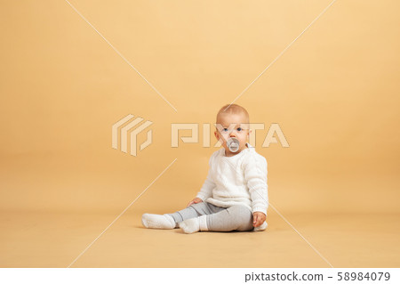 a baby sits on an orange background and looks at the camera 58984079