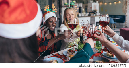 Friends celebrating Christmas or New Year eve clink glasses sitting at the table. 58984755