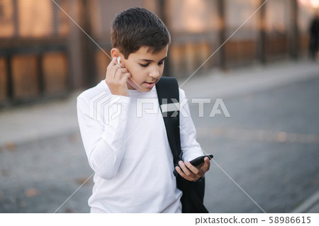 Teenage boy take out a wireless headphones and put then into the ears. Young boy in white shirt with Teenage boy take out a wireless headphones and put then into the ears. Young boy in white shirt with 58986615