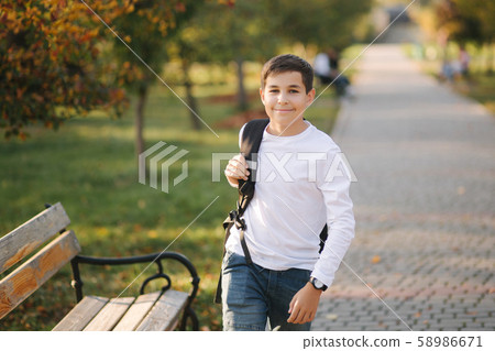 Schoolboy go to school in the morning. Happy teenager in white shirt with black backpack go to study Schoolboy go to school in the morning. Happy teenager in white shirt with black backpack go to study 58986671