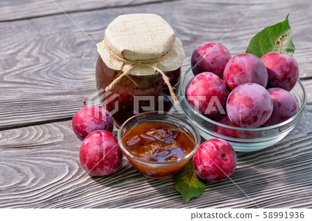 Plum jam in jar and saucer and plums on wooden table 58991936
