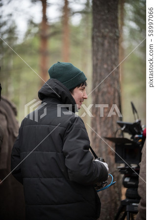 Film director is standing with equipment in hands in the forest near the camera Film director is standing with equipment in hands in the forest near the camera 58997066