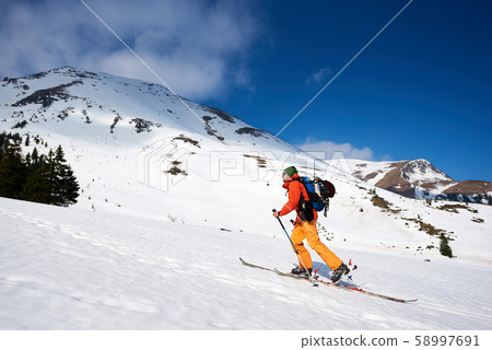 Skier tourist with backpack on background of bright blue sky and beautiful mountain panorama. Skier tourist with backpack on background of bright blue sky and beautiful mountain panorama. 58997691