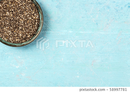 Chia seeds, close-up in a bowl, overhead shot on a blue background with copy space 58997781