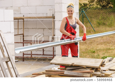 Woman carrying gutter on construction site 58998468