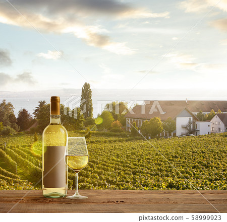 Glass and bottle of wine on wooden rail with country rural scene in background Glass and bottle of wine on wooden rail with country rural scene in background 58999923