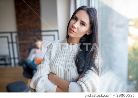 Woman wearing beige sweater standing near window 59000555